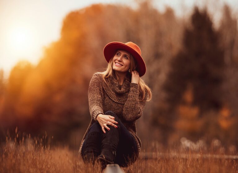 Charming woman in a brown sweater and hat enjoying the fall scenery outdoors.