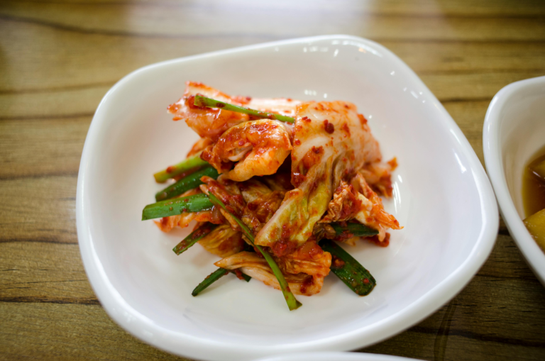Close-up of traditional Korean kimchi served in a white ceramic dish on a wooden table.